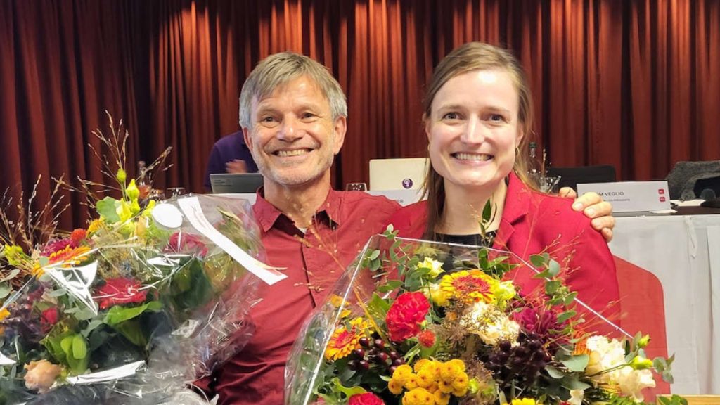 Ueli Egger und Anna Tanner schauen lachend – und je mit einem grossen Blumenstrauss in der Hand – in die Kamera.